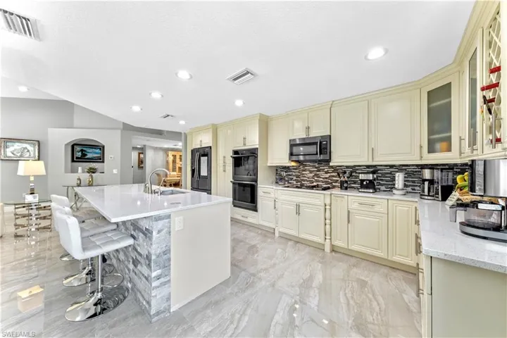 Kitchen with sink, cream cabinetry, a kitchen breakfast bar, refrigerator with ice dispenser, and light stone countertops