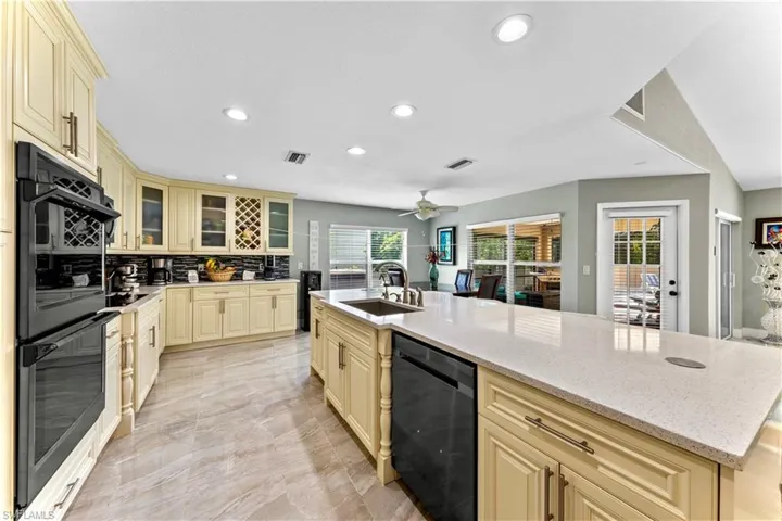 Kitchen featuring decorative backsplash, light stone countertops, ceiling fan, a center island with sink, and sink
