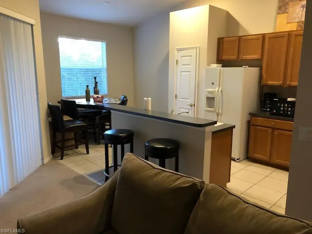 Kitchen featuring dark countertops, brown cabinets, a kitchen bar, white fridge with ice dispenser, and light tile patterned floors