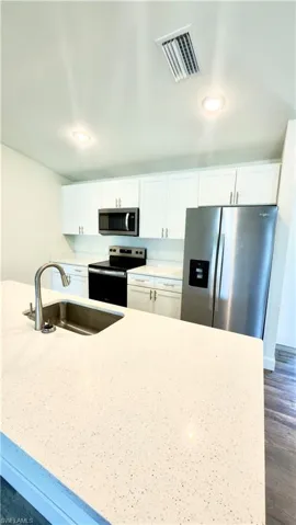 Contemporary kitchen featuring white cabinetry, light-toned countertops, a stainless steel sink with a gooseneck faucet, and recessed lighting
