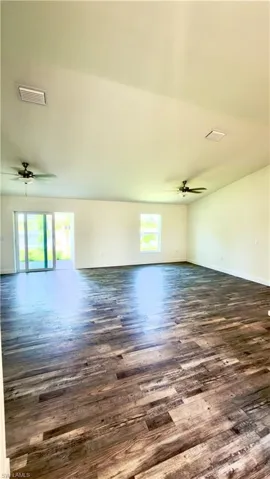 Spacious interior room featuring wood-finish flooring, vaulted ceilings, and two ceiling fans with lighting