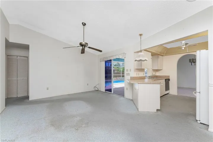 Unfurnished living room with ceiling fan with notable chandelier, tile patterned flooring, and vaulted ceiling