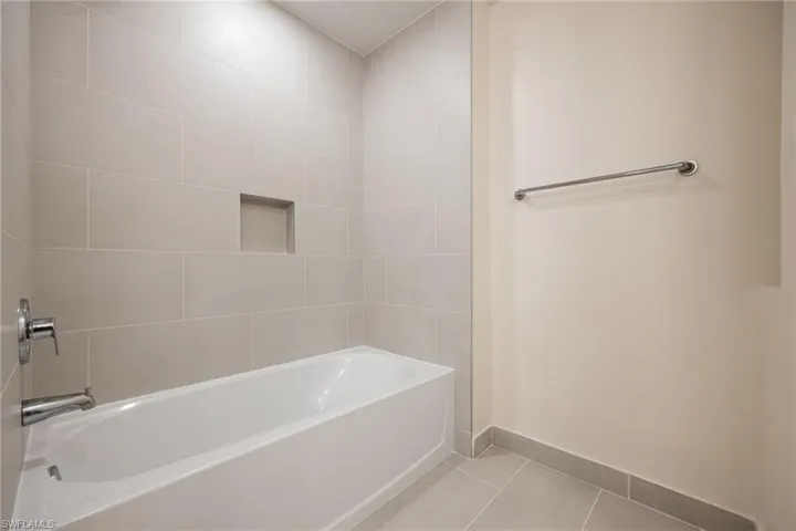 Full bath with baseboards, tile patterned flooring, and washtub / shower combination