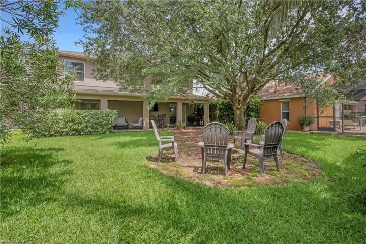 Spacious backyard featuring a large mature tree providing natural shade, a covered patio, and a separate screened-in lanai