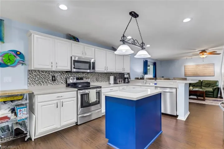Contemporary kitchen featuring a bright blue island with a built-in cooktop, white cabinetry, stainless steel appliances, and wood-finish flooring