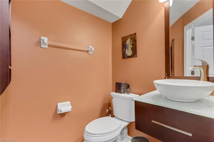 Powder room featuring a vessel sink, floating vanity with a glass countertop, wood-finish mirror, and a modern toilet