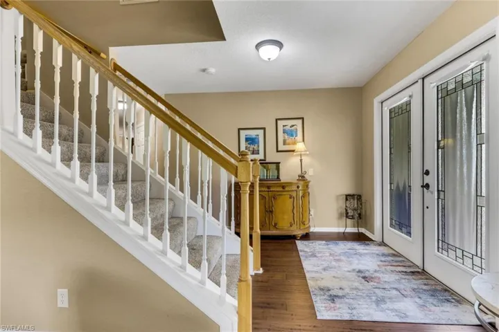 Foyer showcasing wood-finish flooring, a carpeted staircase with white balusters and a wood handrail, and double entry doors with decorative glass inserts