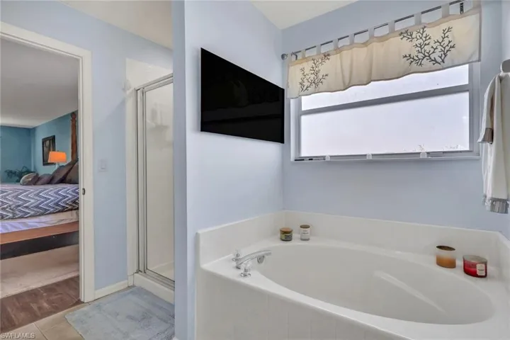 Bathroom featuring a built-in soaking tub, a separate shower enclosure with a glass door, and a wall-mounted television