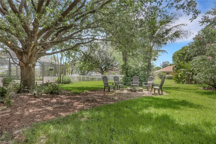 Expansive backyard featuring a lush lawn, mature trees, and a dedicated fire pit area