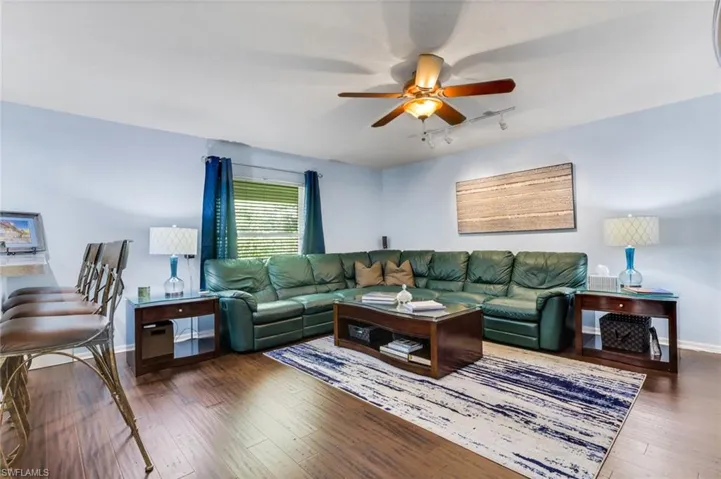 Spacious living area featuring wood-finish flooring, a ceiling fan with integrated lighting, and a large window