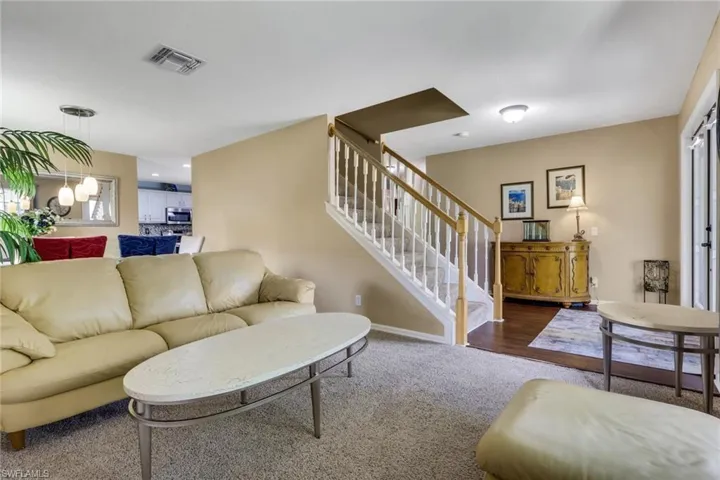 Carpeted living area with a visible staircase featuring white risers and wood-finish handrails