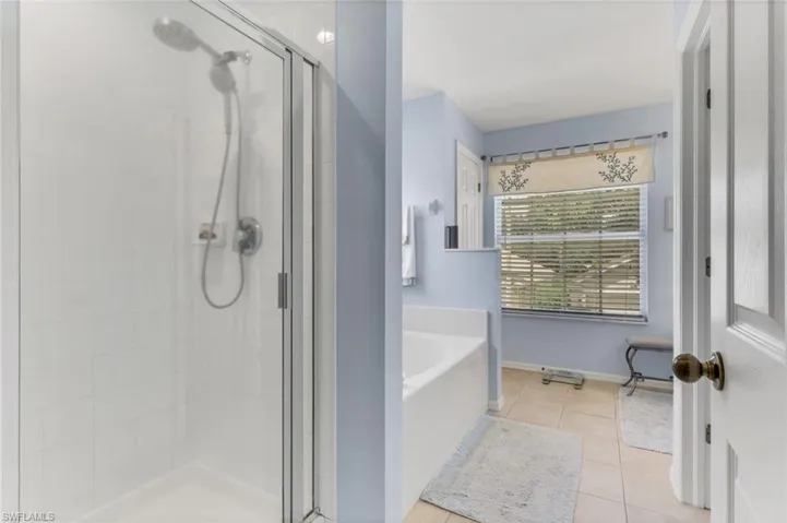 Shower enclosure with glass door and rain shower head, featuring white subway tile surround and a built-in shelf