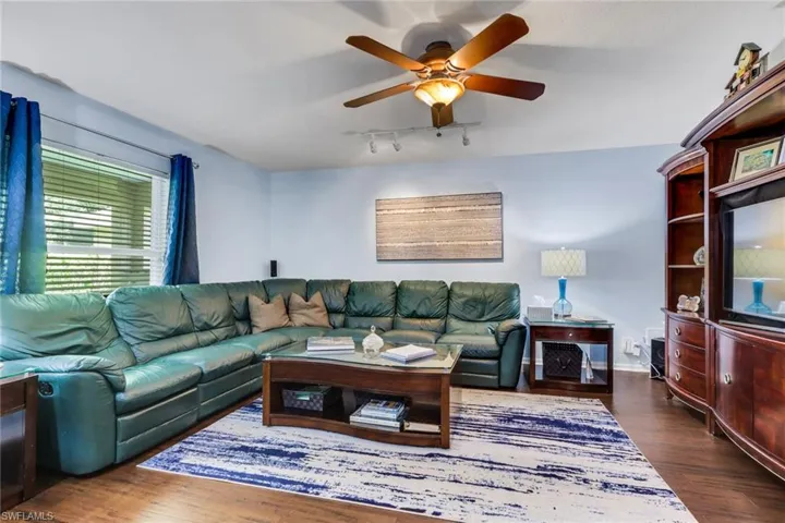 Living area featuring wood-finish flooring, a ceiling fan with light fixture, and a window with blinds
