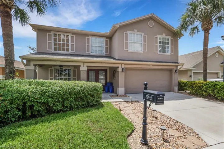 Two-story stucco residence featuring a two-car garage, covered porch entry, and decorative window shutters