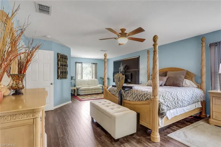 Spacious interior featuring wood-finish flooring, light blue wall paint, a ceiling fan with integrated lighting, and a separate sitting area with natural light from multiple windows