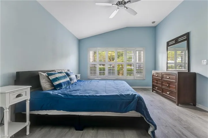 Bedroom with light wood-style flooring, multiple windows, vaulted ceiling, and baseboards