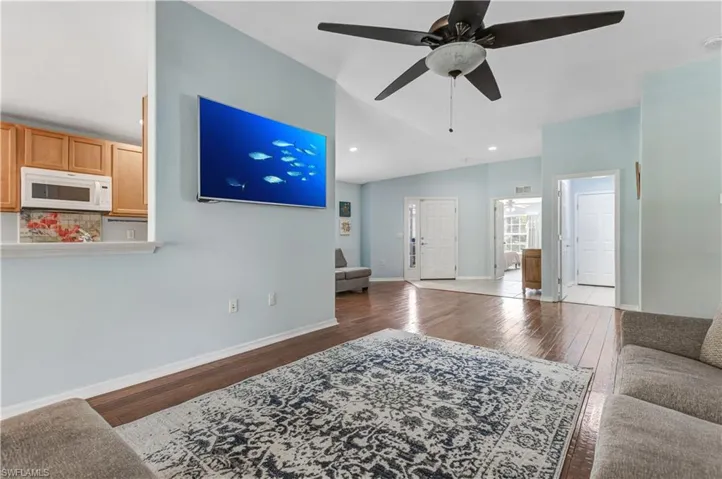Living room with ceiling fan, wood finished floors, vaulted ceiling, baseboards, and recessed lighting
