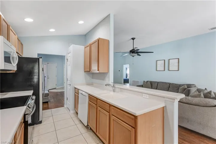 Kitchen with white appliances, open floor plan, a peninsula, a sink, and a ceiling fan