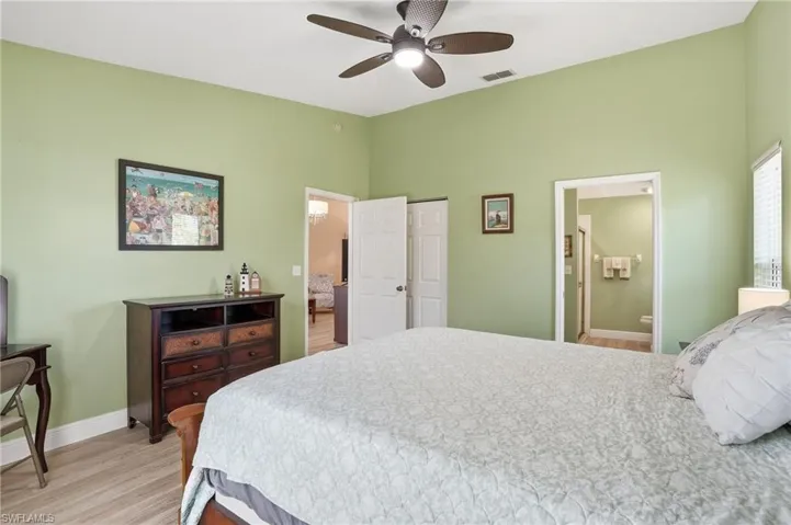 Bedroom with light wood-style floors, a closet, ensuite bath, and a ceiling fan