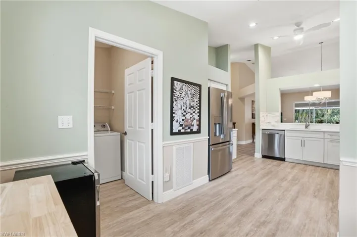 Kitchen featuring stainless steel appliances, washer / dryer, light wood finished floors, white cabinetry, and a high ceiling