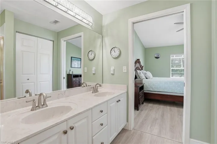 Ensuite bathroom featuring double vanity, light wood finished floors, and a closet