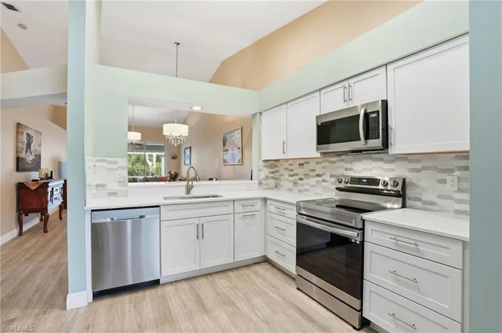 Kitchen with stainless steel appliances, decorative backsplash, white cabinetry, light wood-style floors, and lofted ceiling