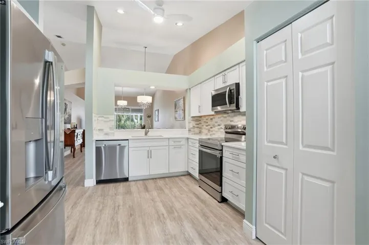 Kitchen featuring stainless steel appliances, white cabinetry, decorative backsplash, light wood-style floors, and a ceiling fan