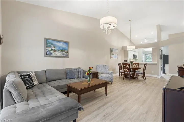 Living room with lofted ceiling, light wood-style flooring, and suspended lighting