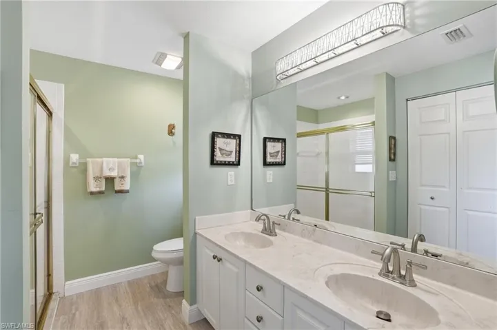 Full bath with double vanity, a shower with shower door, light wood-type flooring, and a closet