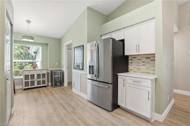 Kitchen with wine cooler, stainless steel refrigerator with ice dispenser, lofted ceiling, white cabinetry, and light wood-style floors