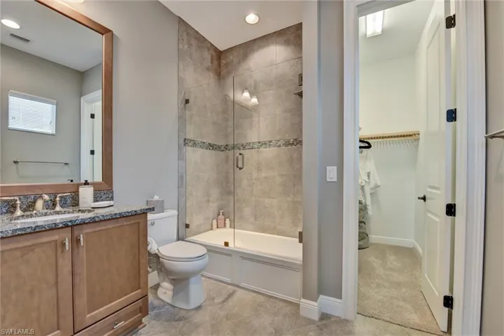 Full bathroom featuring enclosed tub / shower combo, tile floors, toilet, and vanity with extensive cabinet space