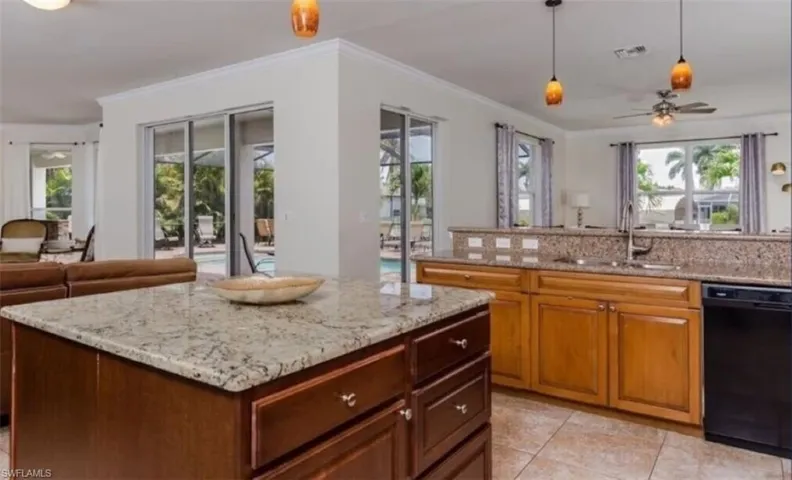 Kitchen featuring light stone countertops, sink, black dishwasher, ceiling fan, and a kitchen island