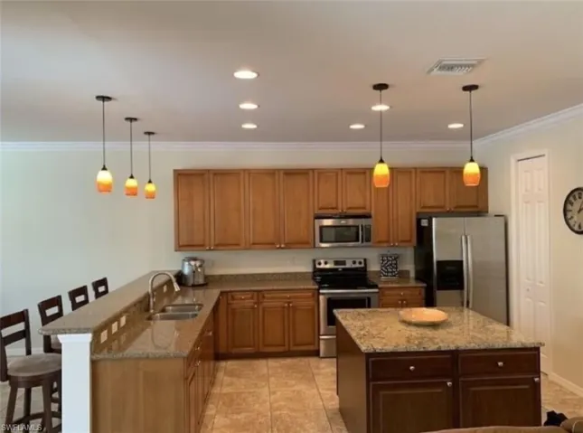 Kitchen with a kitchen bar, stainless steel appliances, sink, and hanging light fixtures