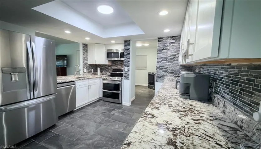 Kitchen with stainless steel appliances, tasteful backsplash, white cabinets, light stone counters, and recessed lighting