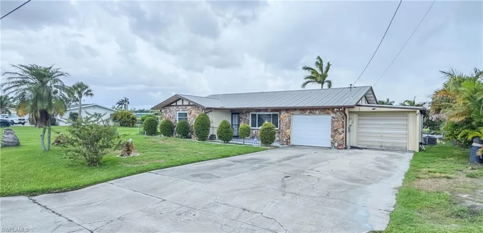 Single story home featuring driveway, a front lawn, a garage, stone siding, and a metal roof