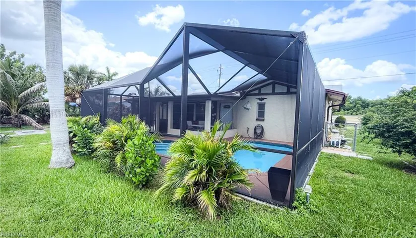 Back of property featuring a yard, a lanai, stucco siding, and an outdoor pool
