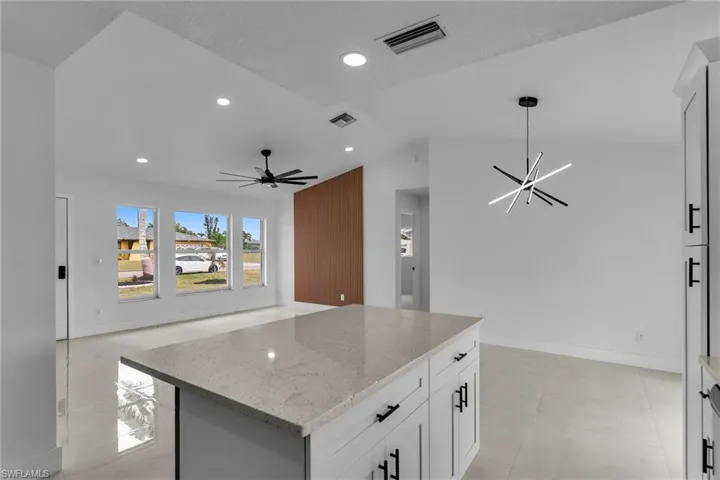 Kitchen featuring decorative light fixtures, a kitchen island, white cabinetry, light stone countertops, and ceiling fan with notable chandelier