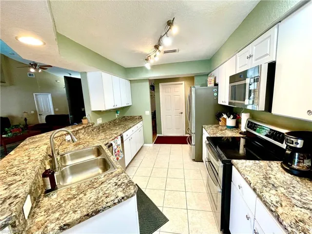 Kitchen featuring appliances with stainless steel finishes, a textured ceiling, sink, light tile patterned floors, and white cabinets