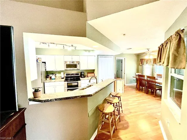 Kitchen with sink, stainless steel appliances, light hardwood / wood-style floors, a kitchen bar, and white cabinets