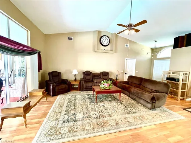 Living room with light hardwood / wood-style floors, high vaulted ceiling, and ceiling fan