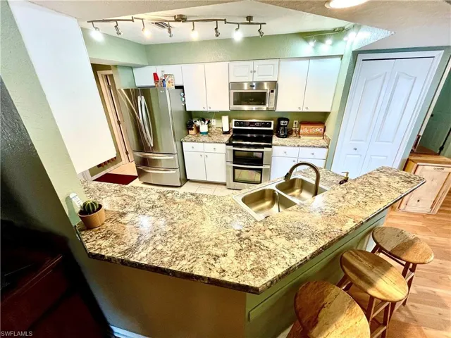 Kitchen with kitchen peninsula, stainless steel appliances, sink, light hardwood / wood-style floors, and white cabinetry