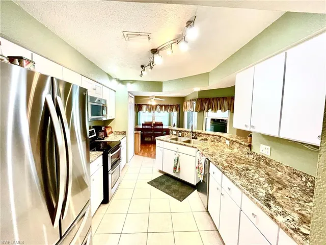 Kitchen with a textured ceiling, stainless steel appliances, ceiling fan, sink, and white cabinets