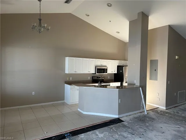 Kitchen featuring white cabinets, high vaulted ceiling, appliances with stainless steel finishes, light tile floors, and pendant lighting