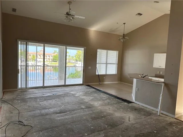 Unfurnished living room featuring high vaulted ceiling and ceiling fan with notable chandelier