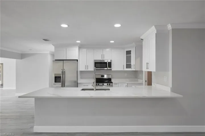 Kitchen featuring stainless steel appliances, ornamental molding, light stone countertops, and white cabinets