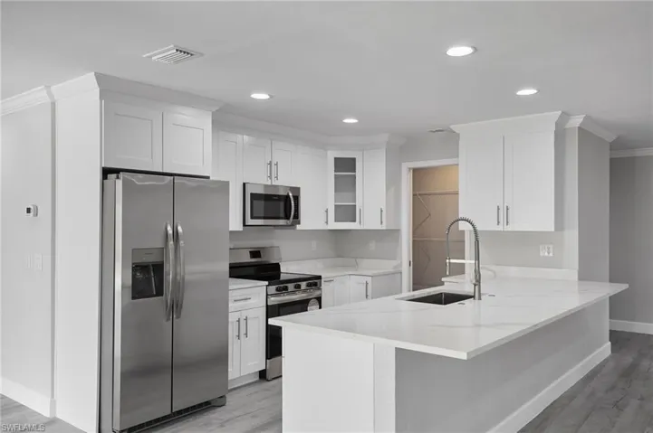 Kitchen featuring stainless steel appliances, white cabinetry, a sink, and a peninsula