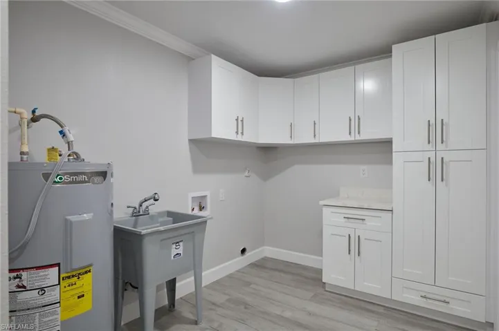 Clothes washing area featuring cabinet space, baseboards, electric water heater, hookup for a washing machine, and light wood-type flooring