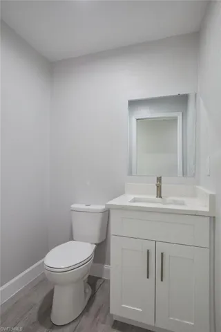 Bathroom featuring toilet, baseboards, wood finished floors, and vanity