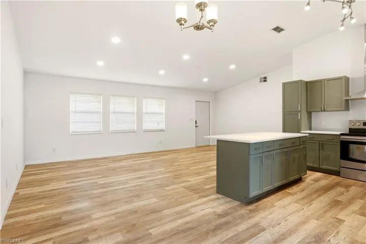 Kitchen with stainless steel electric range, light countertops, green cabinetry, light wood-type flooring, and open floor plan
