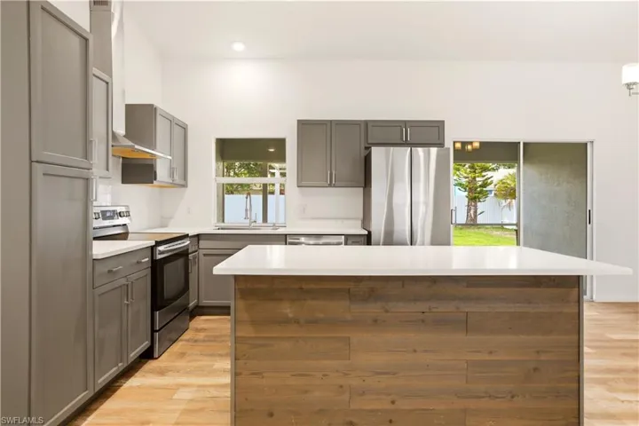 Kitchen with stainless steel appliances, gray cabinets, light countertops, a center island, and recessed lighting